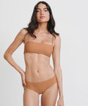 A woman with long dark hair wears the Kumu Bikini Top in terracotta, posing confidently against a plain white background.