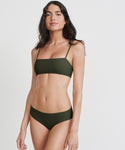 A woman with long dark hair stands confidently against a plain white background, wearing the Kumu Bikini Top in olive green, crafted from recycled nylon.