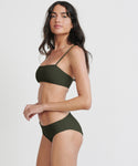 Woman with long dark hair poses in profile against a plain white background, wearing the Kumu Bikini Top by Mikoh in olive green, made from recycled nylon, and looking at the camera.
