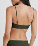 A woman is shown from the back wearing the Kumu Bikini Top in olive green with adjustable straps, made from recycled nylon. Her long brown hair is partially visible against a plain white background.