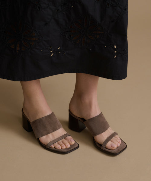 Brown sandals worn with a black dress on a beige background
