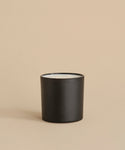 A Large Cedar Glass Candle, 28oz in black matte finish with two unlit wicks, rests elegantly on a neutral beige surface—an ideal piece for any sophisticated setting.
