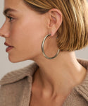 A woman with short blonde hair is shown in profile wearing Large Everyday Hoops and two small gold studs. Paired with a beige knit top against a neutral background, these lightweight hoops are perfect for everyday wear.