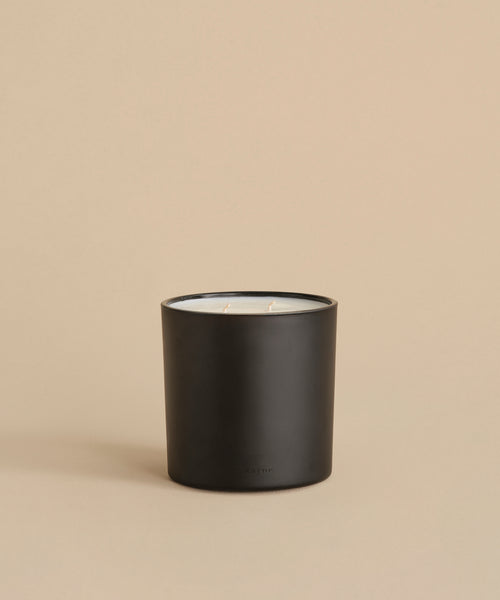 The Large Sun Valley Glass Candle is a black matte cylindrical holder with a white wax candle and two wicks, hand-poured in Los Angeles, shown against a plain beige background.