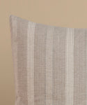 A cream and natural stripe pillow against a beige background.