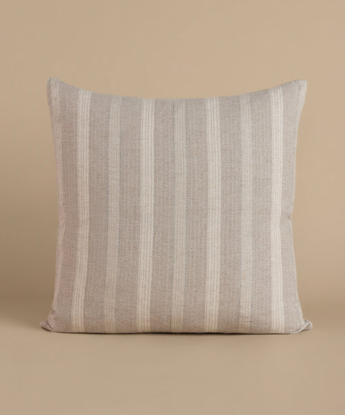 A cream and natural stripe pillow against a beige background.