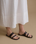 Person wearing black sandals and a white textured skirt on a beige background
