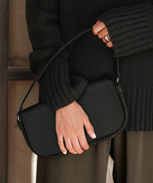 Someone, visible from hands to torso and dressed in a dark knit sweater with olive green pants, holds the Brooke Shoulder Bag, distinguished by its Vachetta leather and short strap.