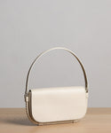The Brooke Shoulder Bag showcases a minimalist design with a cream finish, curved top handle, and flap closure, plus subtle rope detailing. Crafted from premium Vachetta leather in Italy for timeless elegance.