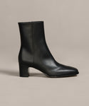 The Leather Bobby Boot, crafted from black Italian leather with a mid-height block heel, rounded square toe, and side zipper, is shown against a neutral beige background.