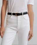 A person wears a white short-sleeve shirt tucked into high-waisted white jeans, accessorized with the Classic Belt—a nappa leather accessory with a gold buckle. Only their torso and upper legs are shown.