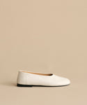 The Leather Elodie Flat is a minimalist Italian-made leather shoe with a rounded toe, black sole, and feminine silhouette, shown against a light beige background.