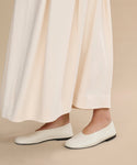 Only the lower legs and feet are visible as someone stands on a beige floor, wearing a long cream-colored skirt paired with Leather Elodie Flats.