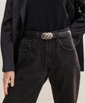 A person wearing high-waisted black jeans with a tucked-in black top, a black blazer, and the Leather Jules Belt featuring a silver swirl rope-twist buckle, with one hand in their pocket.