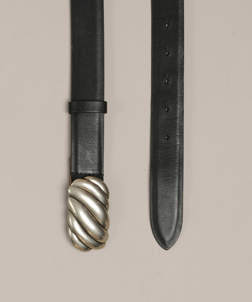 The Leather Jules Belt is shown flat on a light beige background, featuring a black leather strap with multiple adjustment holes and a rope-twist buckle inspired by vintage silver jewelry.