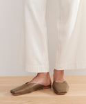 A person stands on a light wooden floor wearing cream wide-leg pants and the Mia Mule—light brown Italian leather, square-toe slip-ons with a minimalist design and open back.