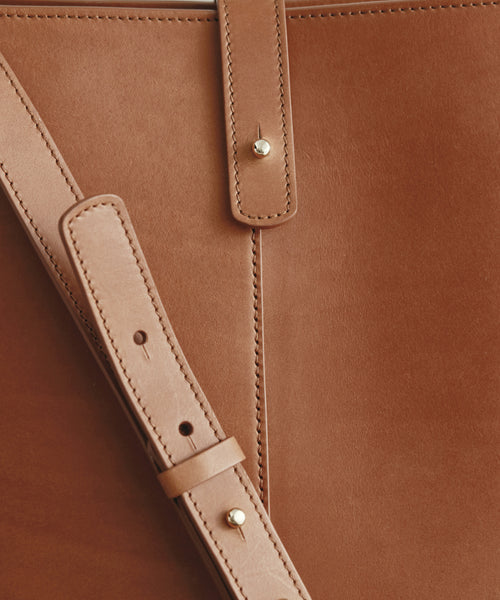 Close-up of the Mini Leather Bucket Bag, handcrafted in Italy from tan leather, featuring fine stitching, a gold hardware strap, and a sleek polished finish.