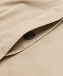 Close-up of the Leo Trench Coat in dark khaki, featuring a dark brown button partially concealed by an overlapping flap of smooth-textured fabric.