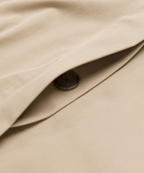 Close-up of the Leo Trench Coat in dark khaki, featuring a dark brown button partially concealed by an overlapping flap of smooth-textured fabric.