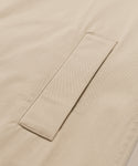 Close-up of a beige fabric with a neatly stitched rectangular flap, likely part of a pocket on the minimalist Leo Trench Coat.
