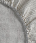 Close-up of the Dusk Linen Fitted Sheet, featuring thin vertical flax stripes and gathered elastic edges, made in Portugal.