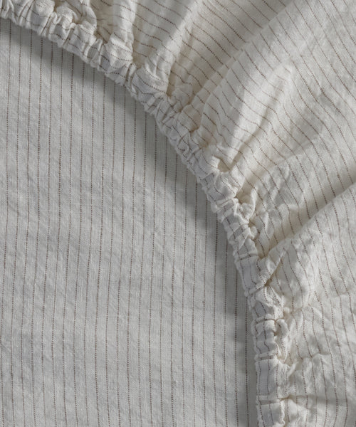 Close-up of the Dusk Linen Fitted Sheet, featuring thin vertical flax stripes and gathered elastic edges, made in Portugal.