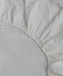 Close-up of the Dusk Linen Fitted Sheet made in Portugal, featuring elastic edges fitted over a mattress corner, showcasing its lightweight linen texture and gathered seams.