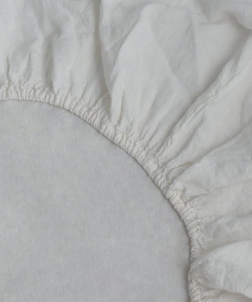 Close-up of the Dusk Linen Fitted Sheet made in Portugal, featuring elastic edges fitted over a mattress corner, showcasing its lightweight linen texture and gathered seams.
