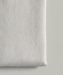 A close-up of the Dusk Linen Flat Sheet, folded in light beige with thin gray pinstripes. Its soft, smooth texture and subtle flax stripe pattern evoke timeless luxury bedding on a light surface.