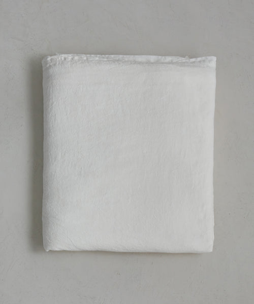 The Dusk Linen Flat Sheet, in crisp white, lies neatly folded on a light gray surface. Its soft, smooth fabric and minimal texture offer understated elegance—ideal for those who love luxurious bedding.