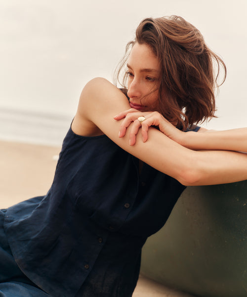 Woman sitting on a beach wearing a blue top and pants.