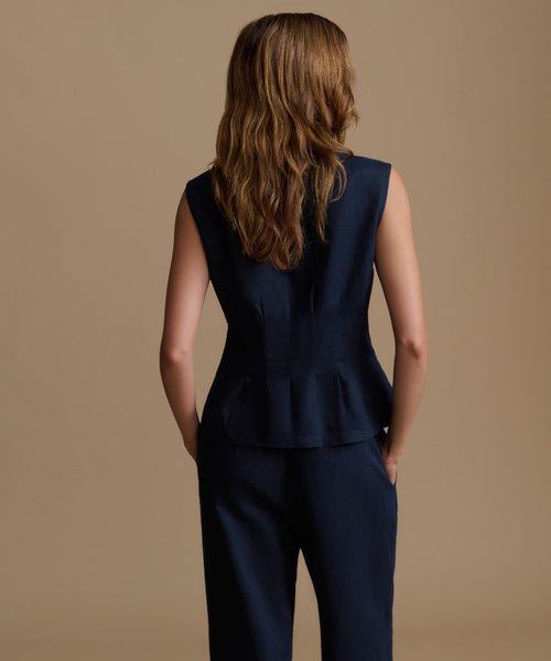 Woman wearing a navy sleeveless top and pants against a beige background