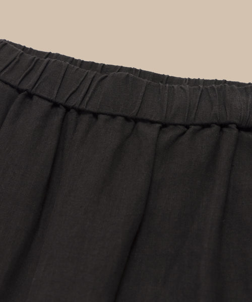 Close-up of the Linen Logan Pant’s black linen waistband with elastic and gathered detailing, shown against a plain beige background—perfect for effortless everyday style.
