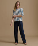 Woman wearing a striped shirt and navy pants on a brown background