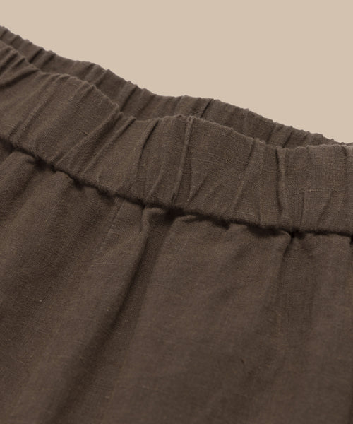 Close-up of the Linen Logan Shorts waistband, featuring an elastic gathering at the top—ideal for warm days—shown against a plain beige background.