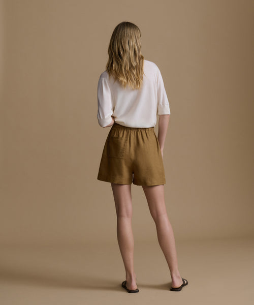 Woman wearing a white shirt and brown shorts against a beige background