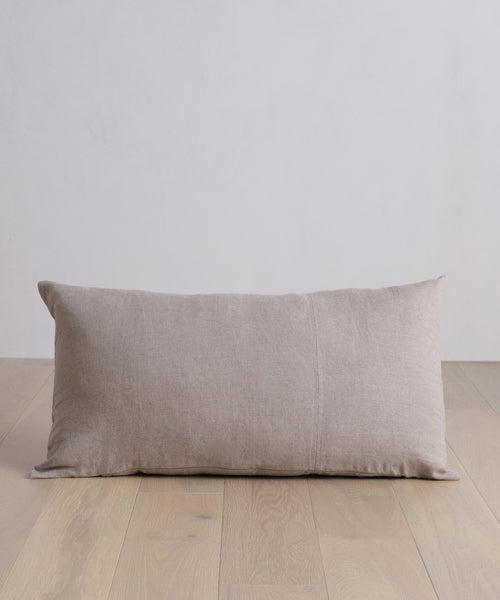The Linen Lumbar Pillow with a feather down insert is placed on a wood floor.