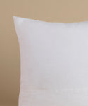 A white linen pillow against a beige background.