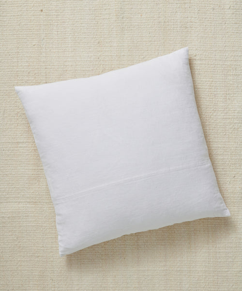 A Linen Pillow in square white design with a feather down insert rests atop a textured beige fabric surface, captured from an overhead angle.