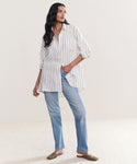 A person stands in a relaxed pose against a plain light background, wearing the Linen Relaxed Oversized Shirt with taupe stripes, light blue jeans, and brown slip-on shoes.