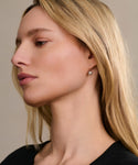 A woman with long blonde hair in a black top is shown in profile against a neutral background, showcasing the Liv Rose Cut Earrings with an elegant, simple round drop design.