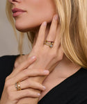 A blonde woman touches her neck and chin, highlighting the Liv Rose Cut Ring along with several gold and gemstone bands on her manicured fingers. Her black top offers a sleek, modern contrast to the jewelry in this close-up shot.