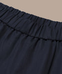 Close-up of the Logan Shorts dark, gathered waistband crafted from lightweight fabric with an elastic waist, shown against a plain beige background.