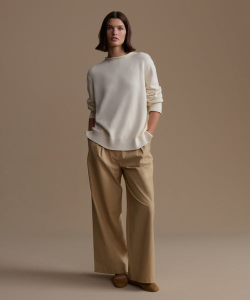 Woman wearing an ivory Loma Pullover and tan pants against a brown background