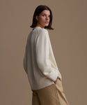 Woman wearing an ivory Loma Pullover and beige pants against a brown background