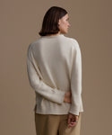 Woman wearing an ivory loma pullover and beige pants against a brown background