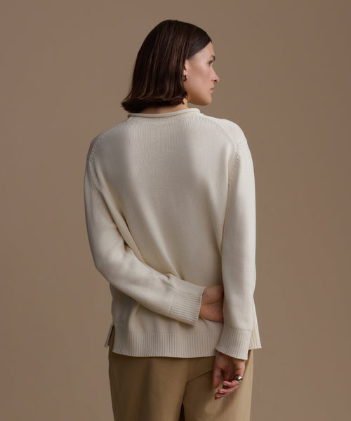 Woman wearing an ivory loma pullover and beige pants against a brown background