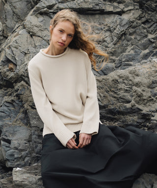 Woman wearing an ivory Loma Pullover and black pants sitting on rocky terrain