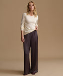 A woman modeling a cream long-sleeve knit top and dark charcoal wide-leg satin pants against a solid beige studio background.