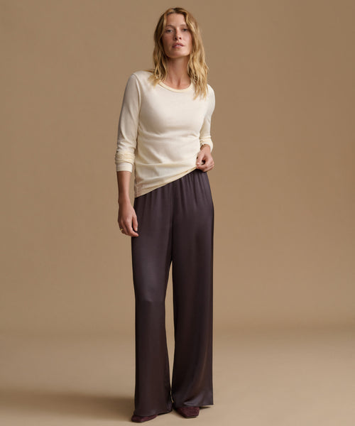 A woman modeling a cream long-sleeve knit top and dark charcoal wide-leg satin pants against a solid beige studio background.